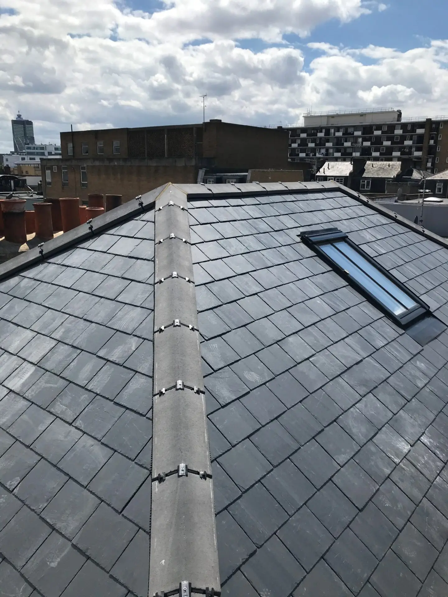 Finished slate hip roof with a roof window, London chimney pots behind