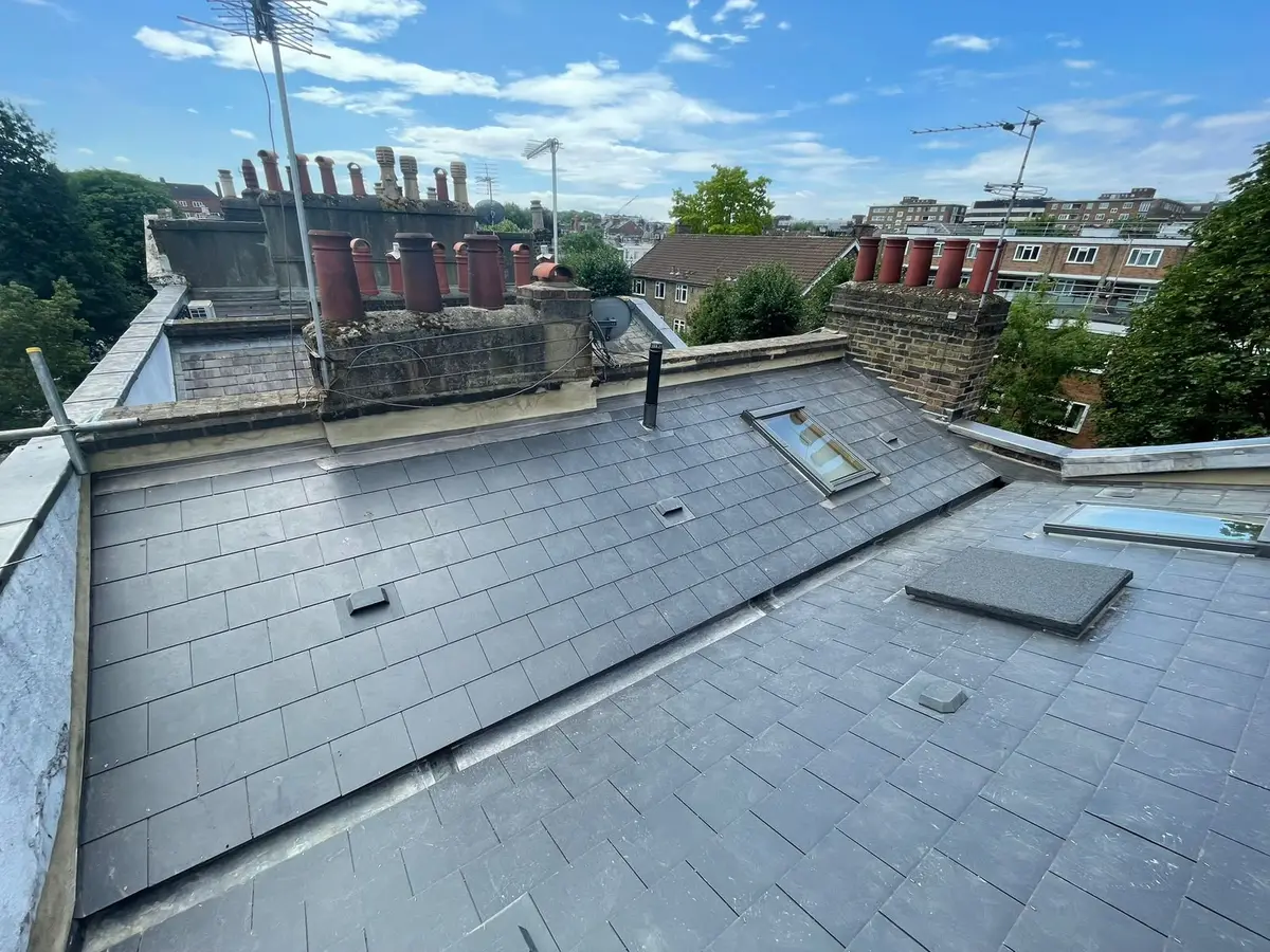 Finished slate roof with a roof window and London chimney pots under a blue sky